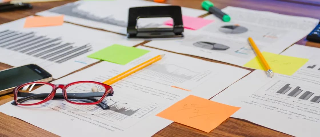 Mesa de trabalho com relatórios impressos, gráficos e anotações
