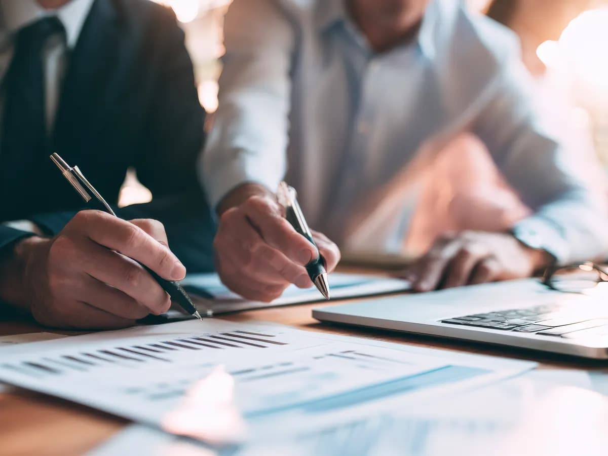 Duas pessoas conferindo relatórios impressos sobre uma mesa de reunião