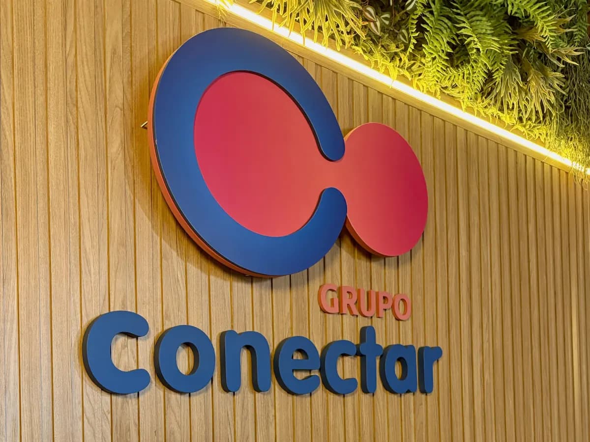 Letreiro do Grupo Conectar na parede da sede, com livros da editora expostos
