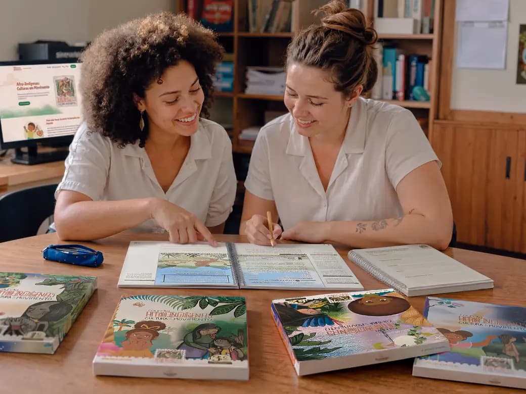 Duas educadoras analisando materiais didáticos sobre uma mesa